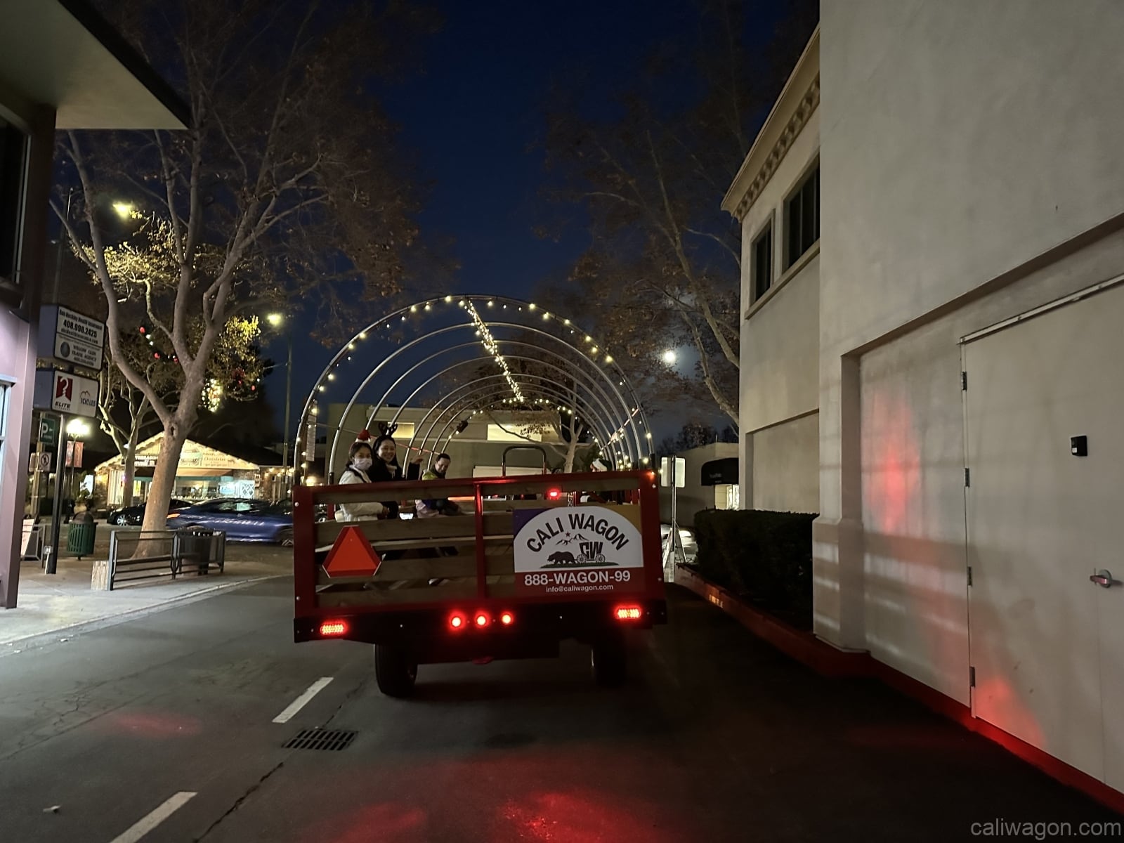 The wagon from behind at night, its hoops strung with lights and the Cali Wagon sign on the tailgate.