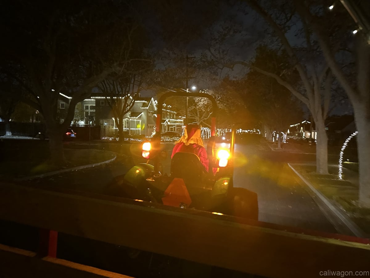 The tractor heading down a street lined with Christmas lights at night, seen from the wagon.