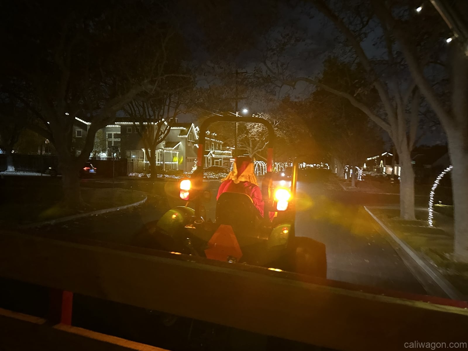 The tractor heading down a street lined with Christmas lights at night, seen from the wagon.