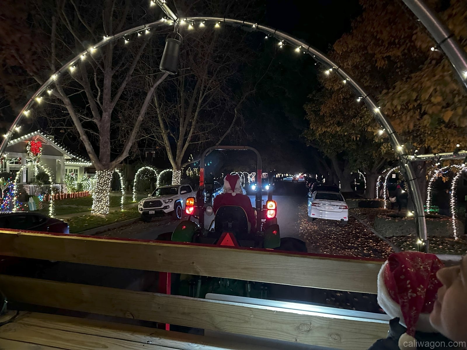 The view from inside the wagon through the lit hoop: the tractor ahead and houses decorated with lights.