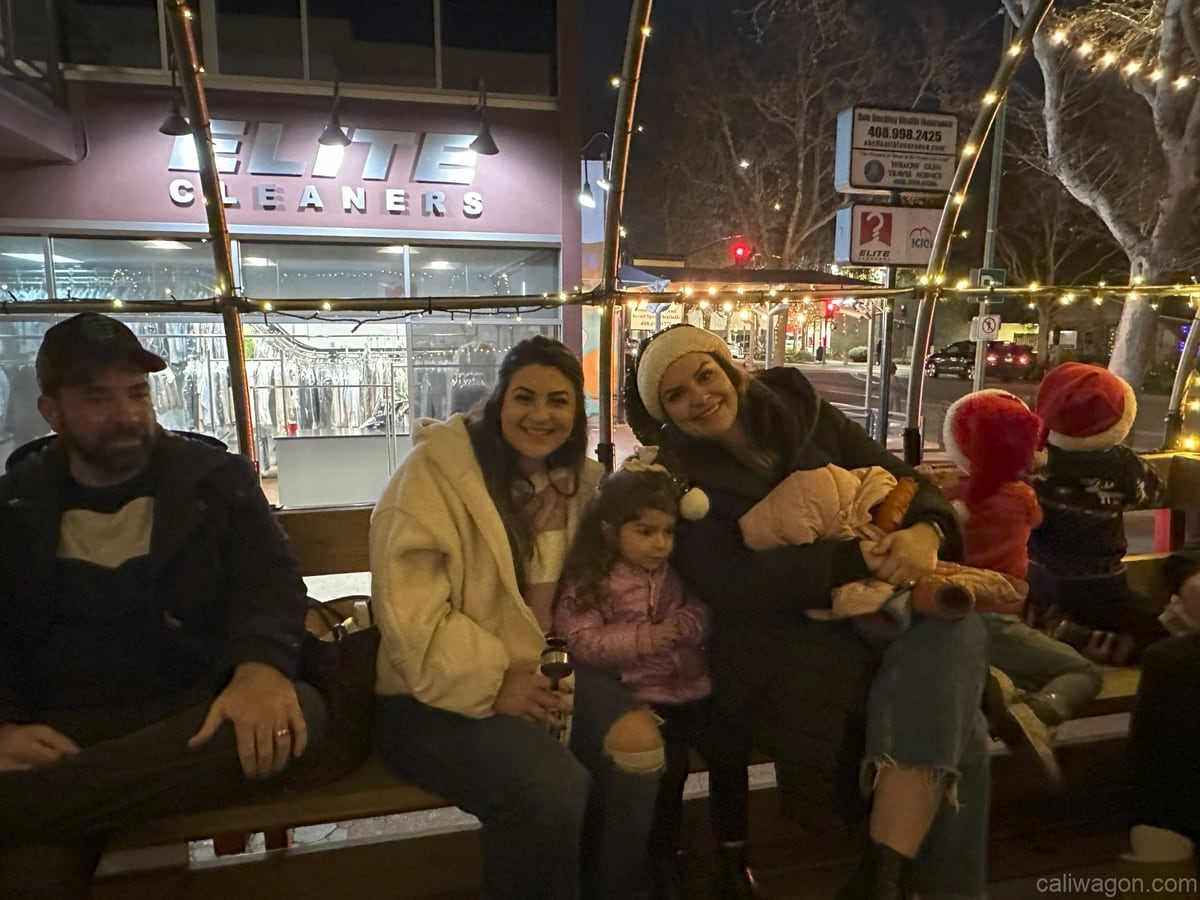 Riders aboard the Cali Wagon under lit hoops on a decorated Willow Glen street, December 2024 (photo 41 of 81)