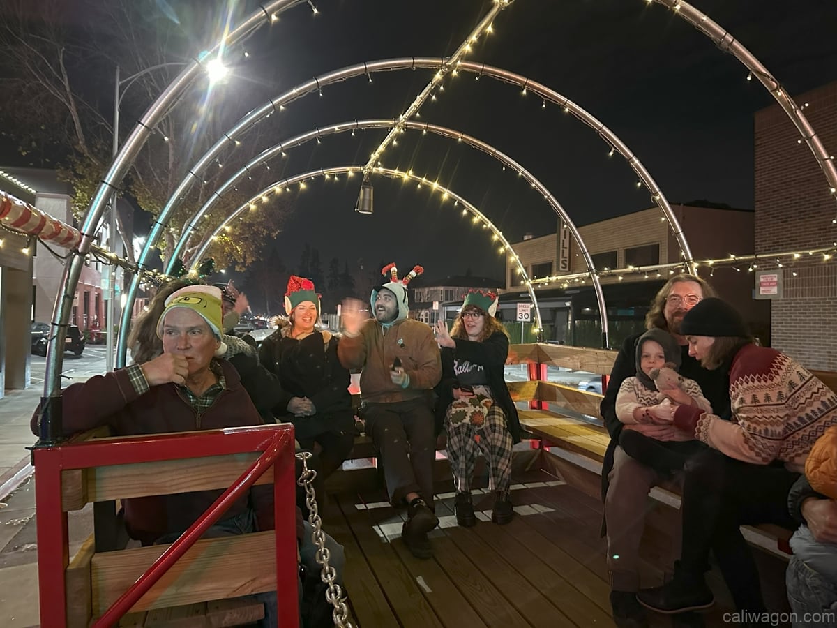 Riders aboard the Cali Wagon under lit hoops on a decorated Willow Glen street, December 2024 (photo 46 of 81)