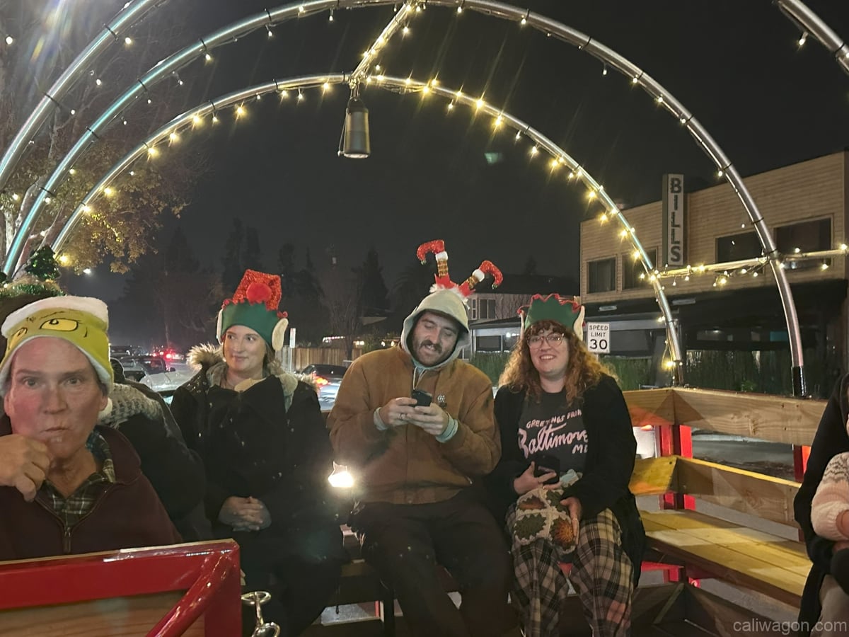 Riders aboard the Cali Wagon under lit hoops on a decorated Willow Glen street, December 2024 (photo 48 of 81)