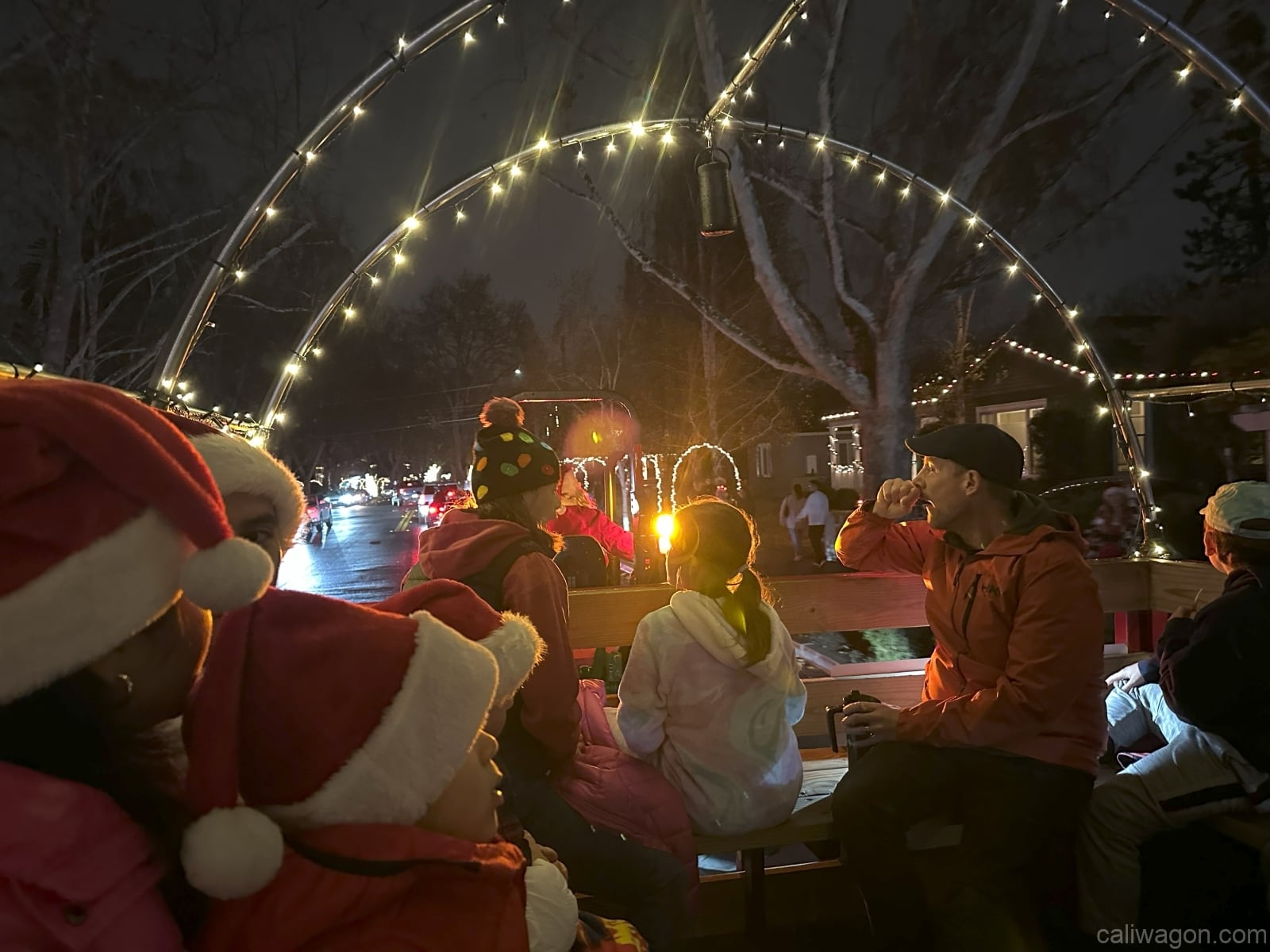 Riders aboard the Cali Wagon under lit hoops on a decorated Willow Glen street, December 2024 (photo 54 of 81)