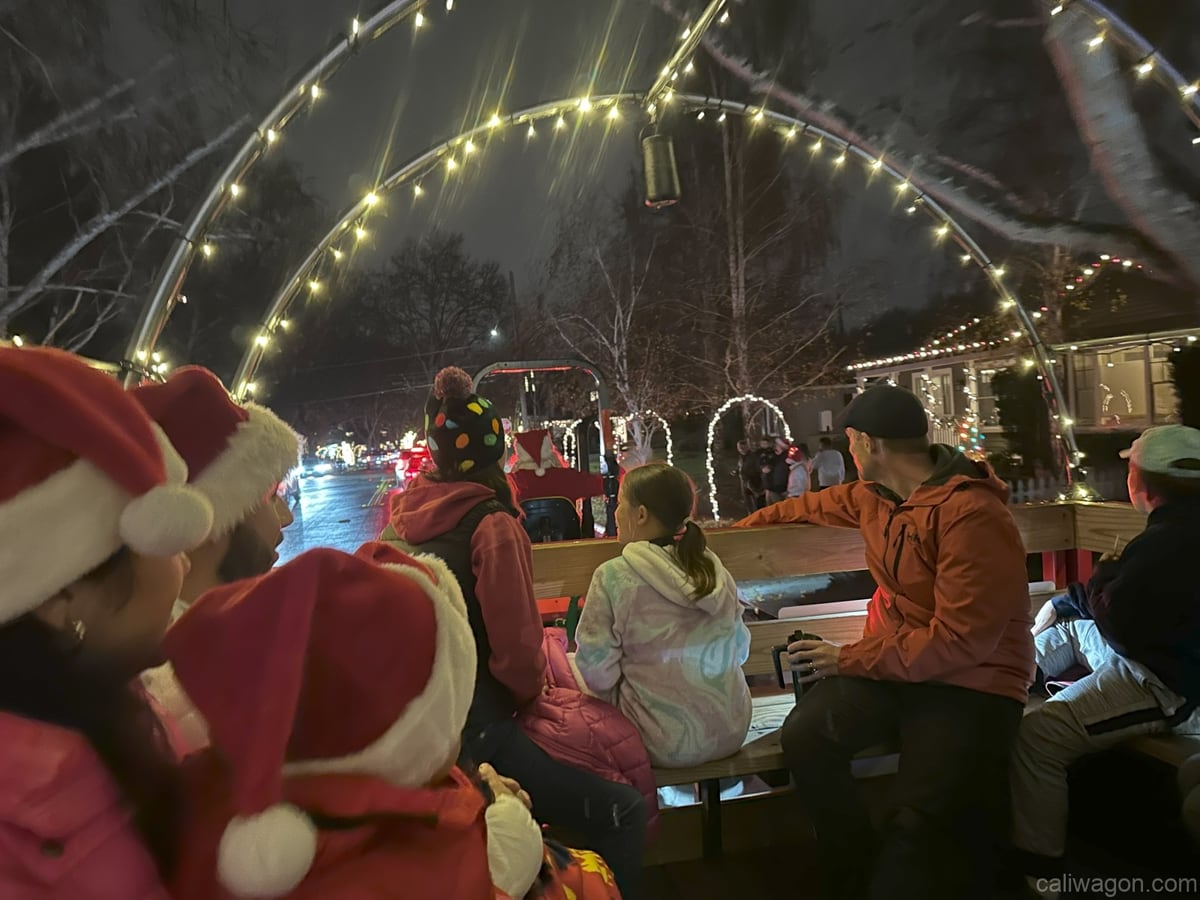 Riders aboard the Cali Wagon under lit hoops on a decorated Willow Glen street, December 2024 (photo 58 of 81)