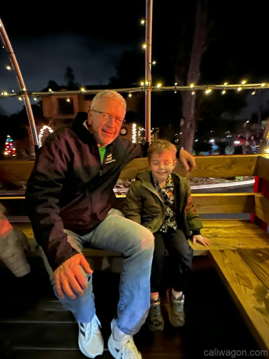 Riders aboard the Cali Wagon under lit hoops on a decorated Willow Glen street, December 2024 (photo 80 of 81)