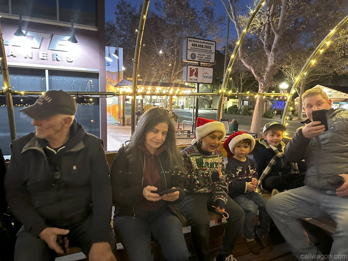 Riders aboard the Cali Wagon under lit hoops on a decorated Willow Glen street, December 2024 (photo 31 of 81)